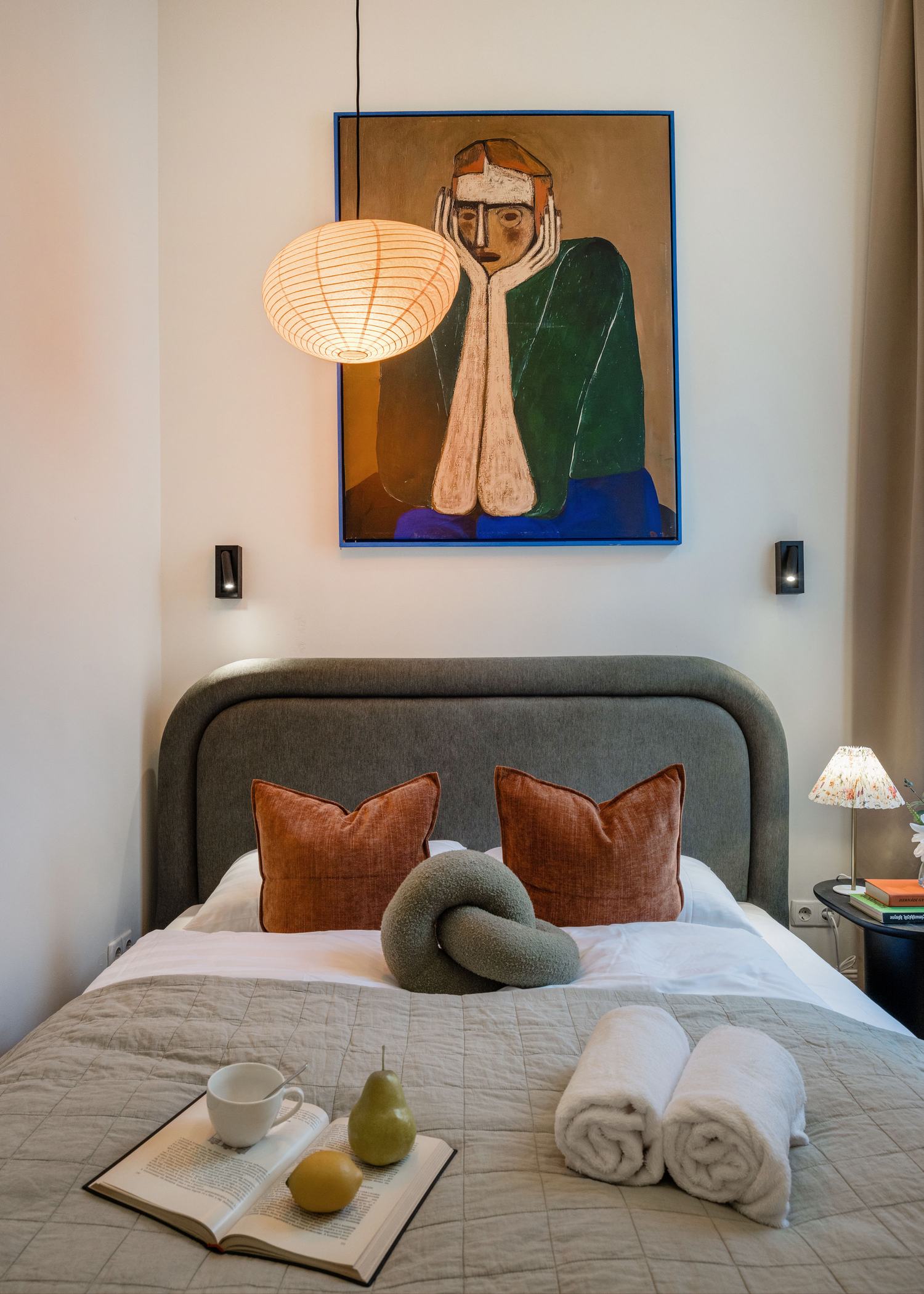 Boutique-style bedroom with grey upholstered headboard and original artwork