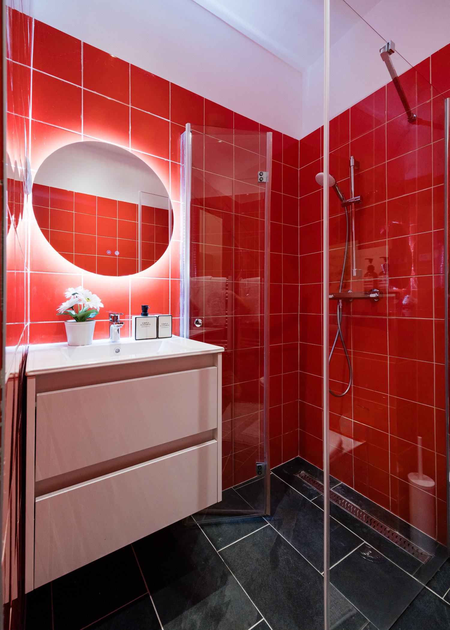 Bold red-tiled bathroom with backlit round mirror